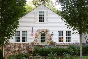 White cottage with stone accents and green front door, plus an American flag