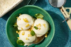 Southern Living Corn Ice Cream in a bowl to serve sprinkled with fresh corn and basil leaves