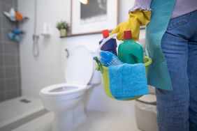 The cleaning woman is standing in the bathroom holding a blue bucket full of chemicals and facilities for storing her hands.