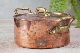 Old copper casserole with lid and brass handles on a concrete background. 