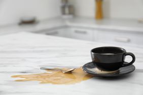 Cup and spilled coffee on white marble table in kitchen